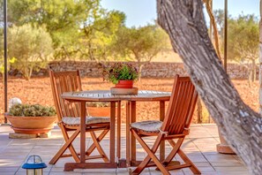 A wooden table and four chairs with cushions, a potted plant, and a lantern on a tiled patio. - Secluded Holiday Home Son Garrot with Garden, Mountain View & Wi-Fi; Parking Available (Santanyí)