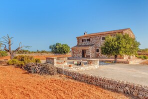 A stone building with a tiled roof, a paved courtyard, and a stone wall. - Secluded Holiday Home Son Garrot with Garden, Mountain View & Wi-Fi; Parking Available (Santanyí)