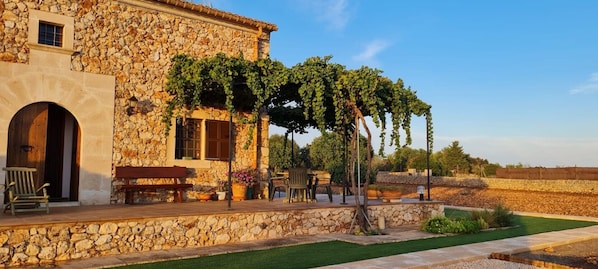 Un bâtiment en pierre doté d’un patio couvert, d’un espace extérieur aménagé pour s’asseoir et d’un vignoble.