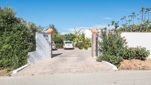 Een oprit die leidt naar een gebouw met een witte gevel, een auto geparkeerd ervoor, en een helderblauwe lucht.