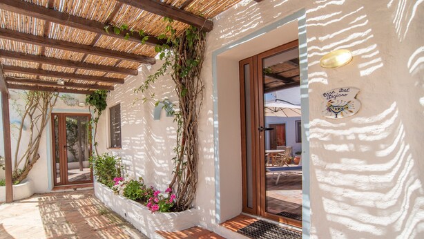 A covered outdoor area with a pergola, a white wall with a door, and a sign reading 'Casa Del Ragiano'.