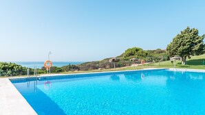 Piscina azul cristalina con un flotador salvavidas, rodeada de vegetación y vista al mar.
