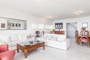 Un salon spacieux avec un canapé blanc, une table basse et un coin repas comprenant une table et des chaises en bois.