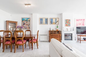 Un espace repas avec des chaises et une table en bois, un canapé, une cheminée et des œuvres d’art murales.