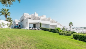 Un edificio moderno blanco con techo plano, una zona de estar exterior cubierta y un césped bien cuidado.