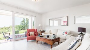 Un salón espacioso con puerta de vidrio a un balcón, un sillón rojo, un sofá blanco y una mesa de centro.
