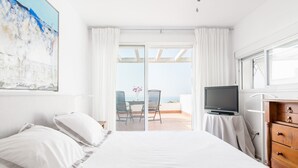 Un dormitorio con cama, televisión, cómoda y balcón con mesa y sillas.