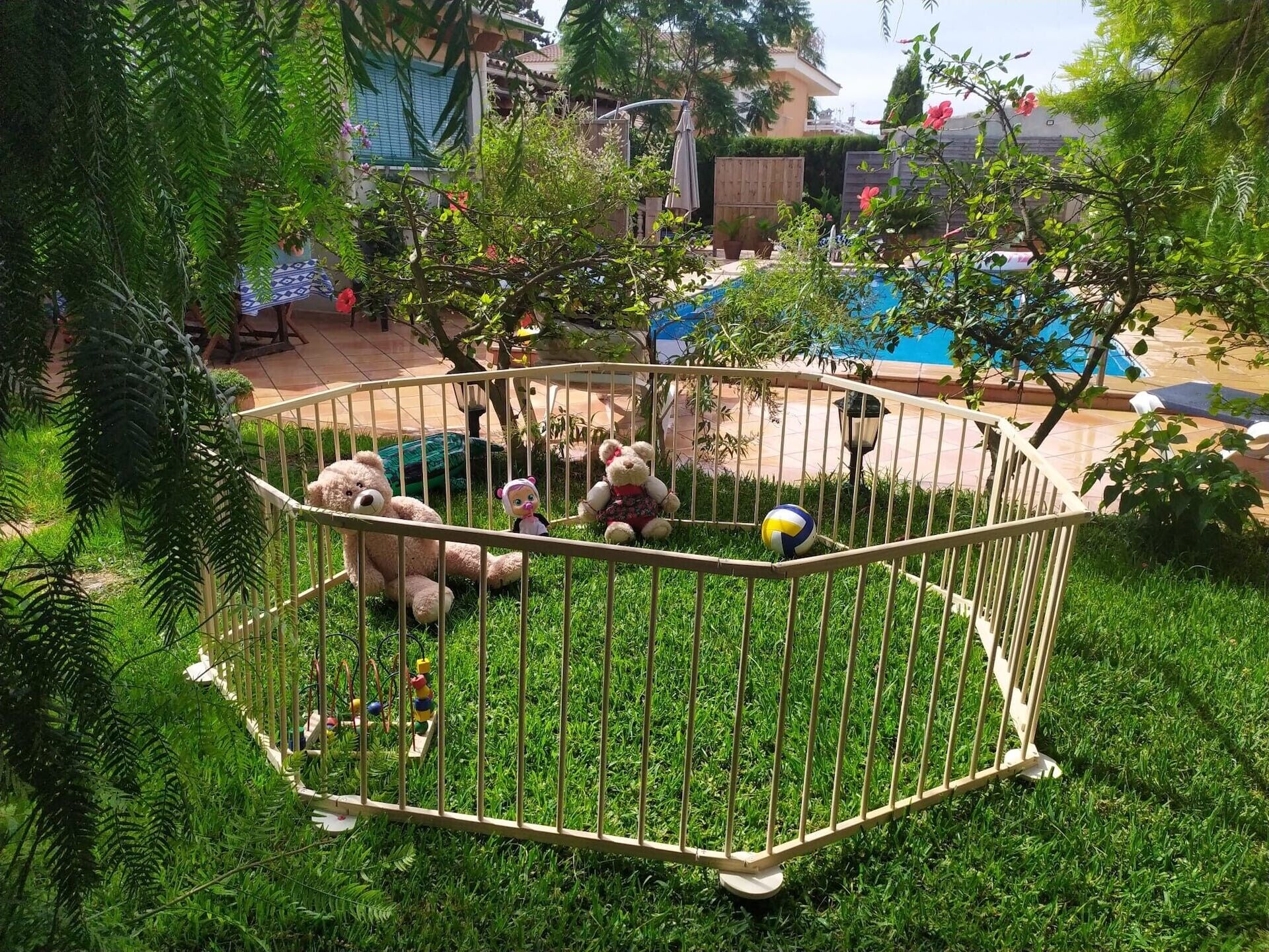 Un'area esterna recintata con piscina, vegetazione e una piccola struttura giochi.