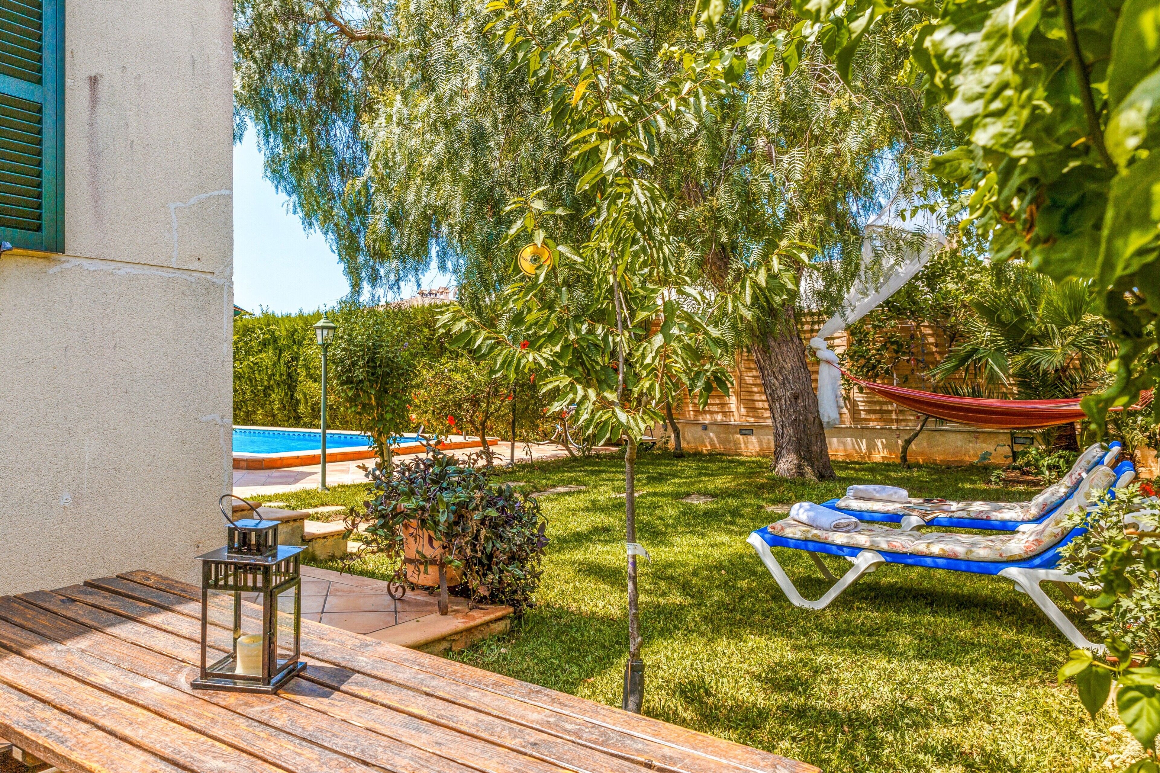 A wooden deck with a lantern, a hammock, and a pool in the background.