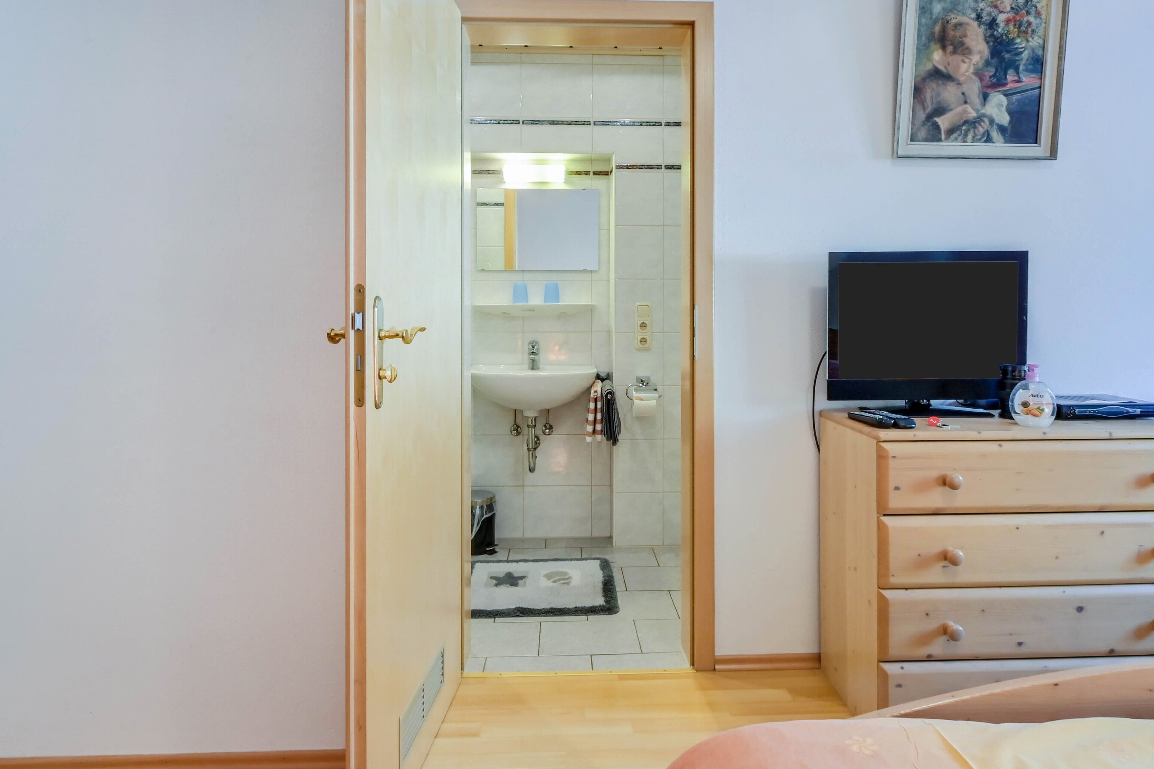 A room with a wooden dresser, a television, and a bathroom visible through an open door.