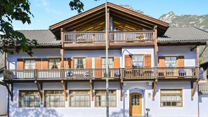A two-story building with wooden balconies, large windows, and a mountain backdrop.