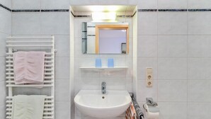 A bathroom with a white sink, a mirror, a towel rack with towels, and a soap dispenser.
