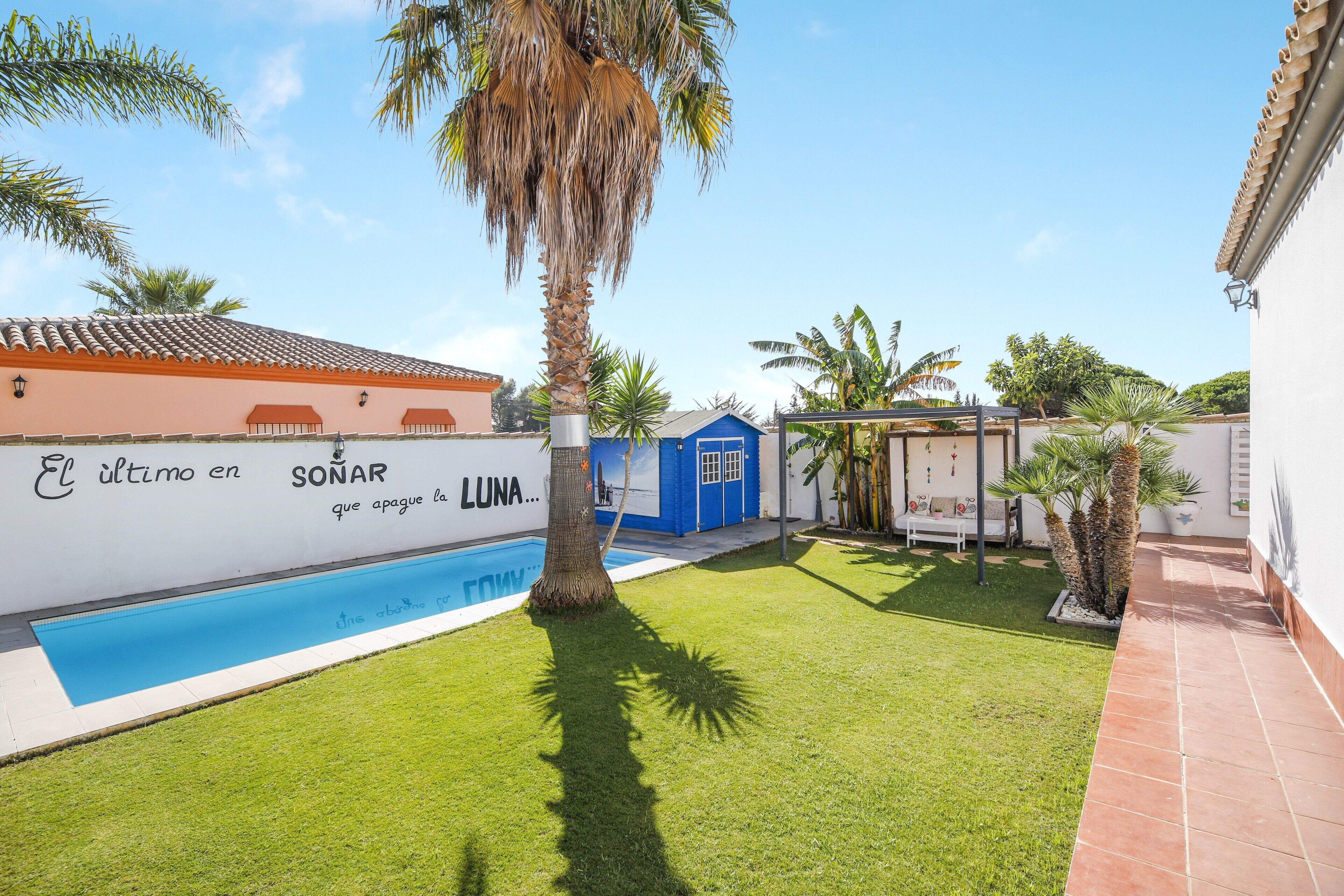 A pool area with a blue pool, a white wall with text, and a blue building.