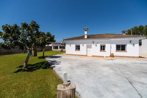 A white building with a tiled roof, a concrete driveway, and a grassy area with trees.