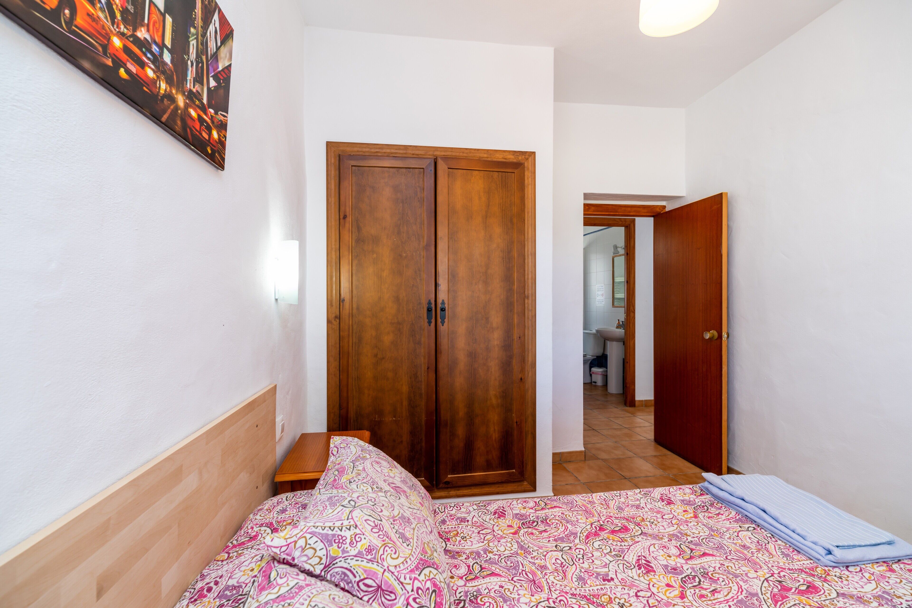 A bedroom with a bed, a wardrobe, and a bathroom visible through an open door.