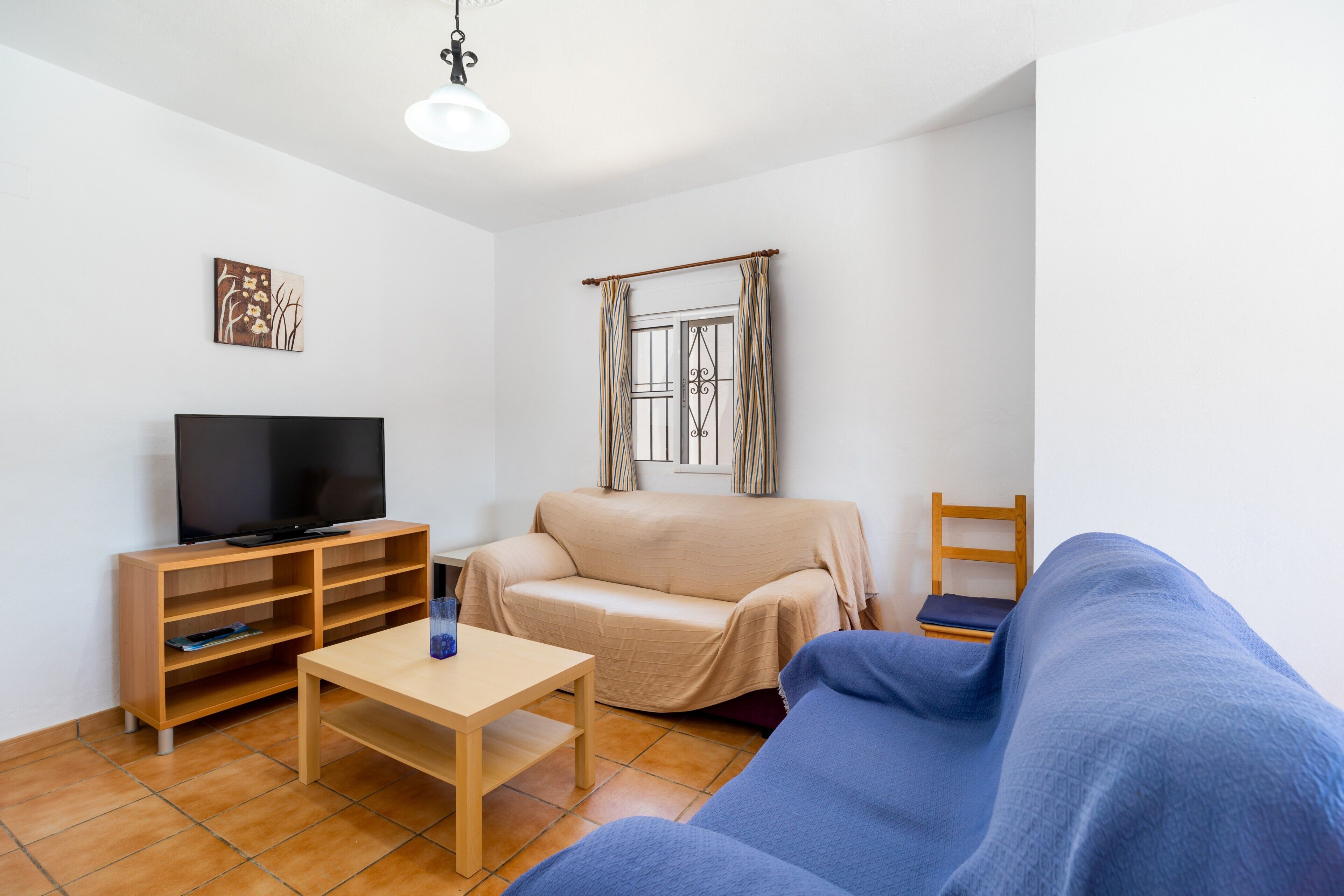 A living room with a TV, a sofa, a coffee table, and a window with curtains.