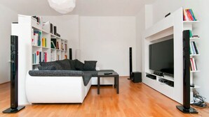 Una sala de estar moderna con un sofá blanco, una mesa de centro, un televisor de pantalla plana y una estantería llena de libros.