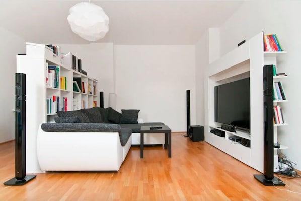 A modern living room with a white sofa, a coffee table, a flat-screen TV, and a bookshelf filled with books.