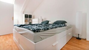 Un dormitorio moderno con techo inclinado, una cama con colcha estampada, una mesita de noche, una lámpara y un armario.