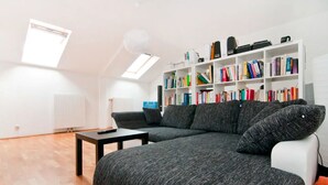 Una sala de estar moderna con un sofá seccional, una estantería blanca llena de libros, una mesita y un radiador.