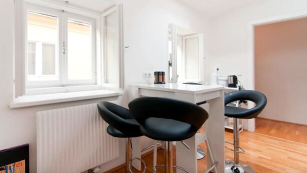 Una habitación moderna con un radiador blanco, una ventana con persianas, un escritorio blanco con una silla y un espejo.