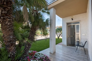 Un espace extérieur abrité, avec un palmier, une colonne en béton, une porte et une chaise.