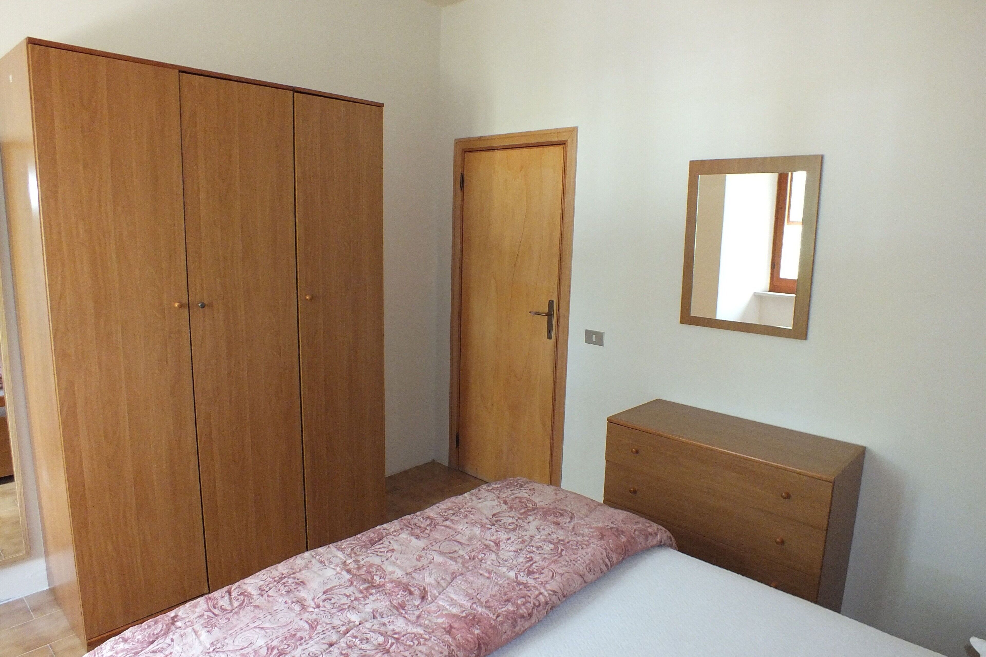 Una camera da letto con un letto, un'armadio in legno, una cassettiera di legno e uno specchio a parete.
