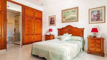 Un dormitorio con un amplio armario de madera, una cama con colcha verde, dos mesitas de noche con lámparas y cuadros enmarcados en las paredes.