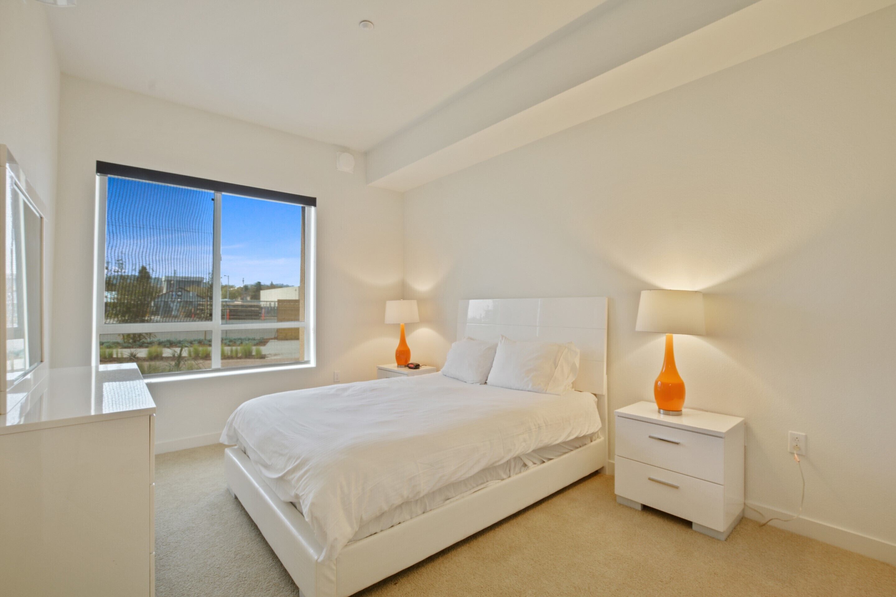 Un dormitorio moderno con una cama grande, dos mesitas de noche y una ventana con vistas al exterior.