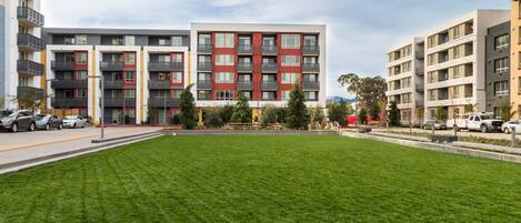 A modern apartment building with multiple balconies, a well-maintained lawn, and a parking area.