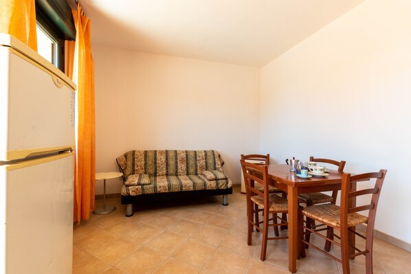 Una habitación pequeña con sofá, una mesa de comedor y sillas, y un refrigerador.