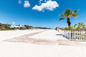Ein Strand mit einer Holzpromenade, Palmen und einem klaren, blauen Himmel.