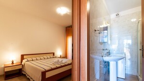 A bedroom with a bed, bedside tables, and a bathroom with a sink and mirror. - Apartment in the city with balcony and a view – Apartment Cavour H (Villasimius)