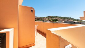 A rooftop terrace with a view of a hillside town, a white chair, and a building with a visible 'H' sign. - Apartment in the city with balcony and a view – Apartment Cavour H (Villasimius)