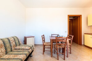 Un salon comprenant un canapé, une table à manger avec des chaises, un petit meuble et une porte donnant sur une autre pièce.