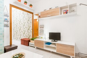 Un salon moderne avec un téléviseur, des meubles blancs et en bois, une plante et une bibliothèque.