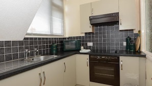 A compact kitchen with a sink, microwave, oven, and a trash bin.
