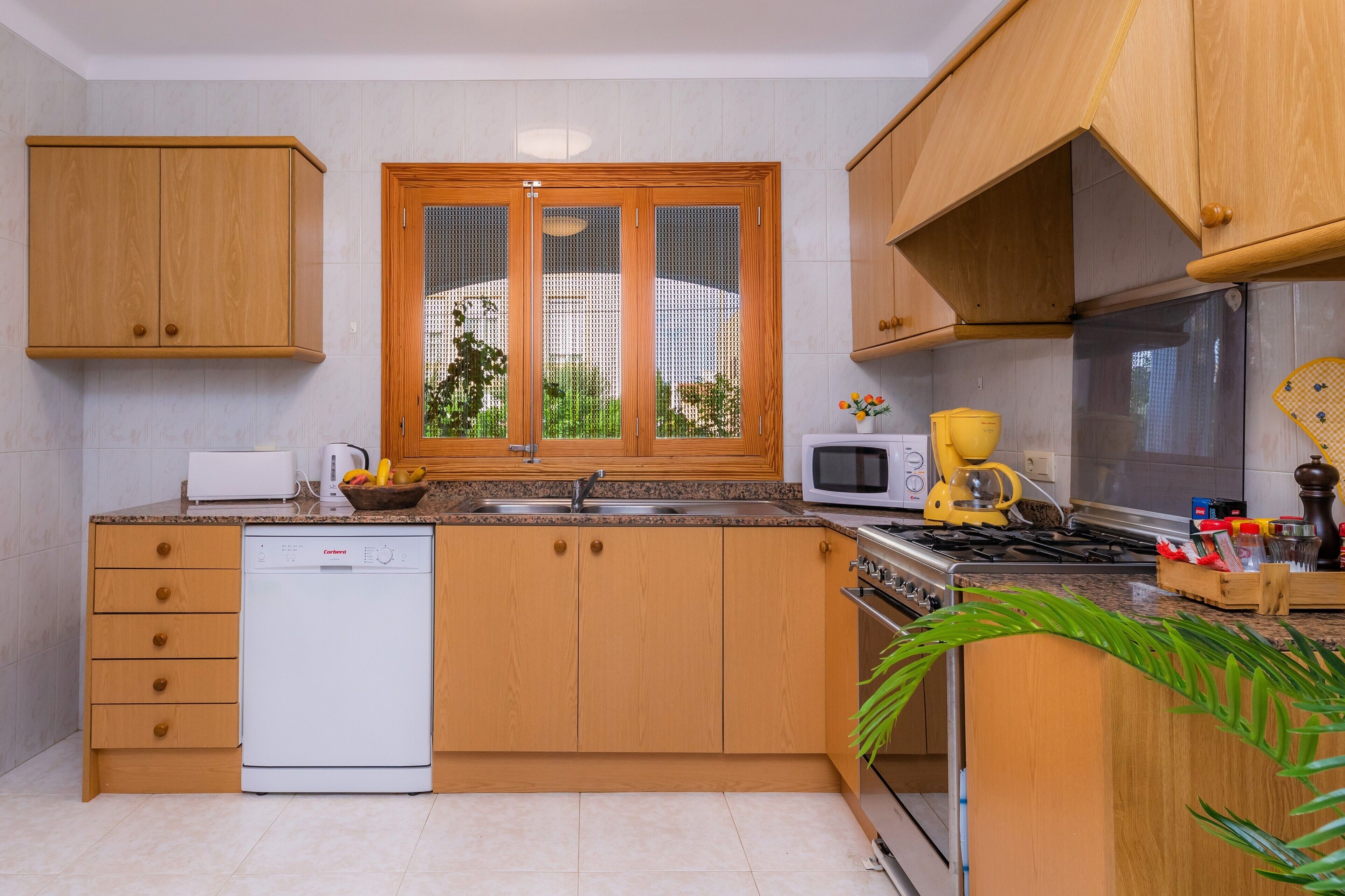 A modern kitchen with wooden cabinets, a dishwasher, a microwave, a stove, and a window with blinds.