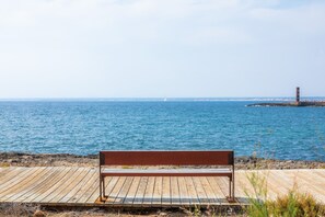A wooden bench on a pier overlooking a calm sea with a lighthouse in the distance.