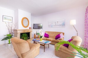 A living room with a sofa, armchairs, a coffee table, a fireplace, a TV, and a painting on the wall.