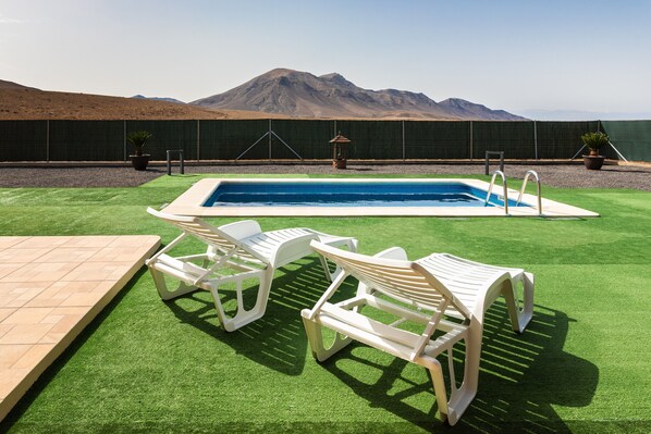A pool area with artificial grass, two white lounge chairs, and a view of mountains.
