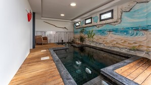 Ein Schwimmbecken mit Holzterrasse und einer Wandmalerei mit Strandmotiv.