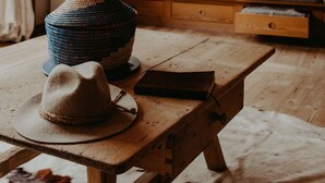 A rustic wooden table with a woven basket and a hat, a sofa with cushions, and a cowhide rug. - Luxurious Chalet with Jacuzzi, Dreamlike Interior, Wi-Fi and Garden (La Valle Agordina)