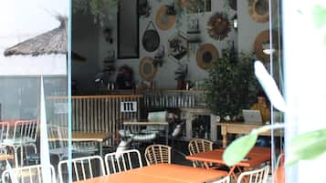 A dining area with a glass partition, white metal chairs, and an orange table.