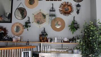 A cozy bar area with a wooden counter, multiple hanging planters, and a variety of wall decorations including mirrors and lanterns.