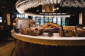 Een bakkerijdisplay met brood en gebak, een kassa en een kroonluchter.
