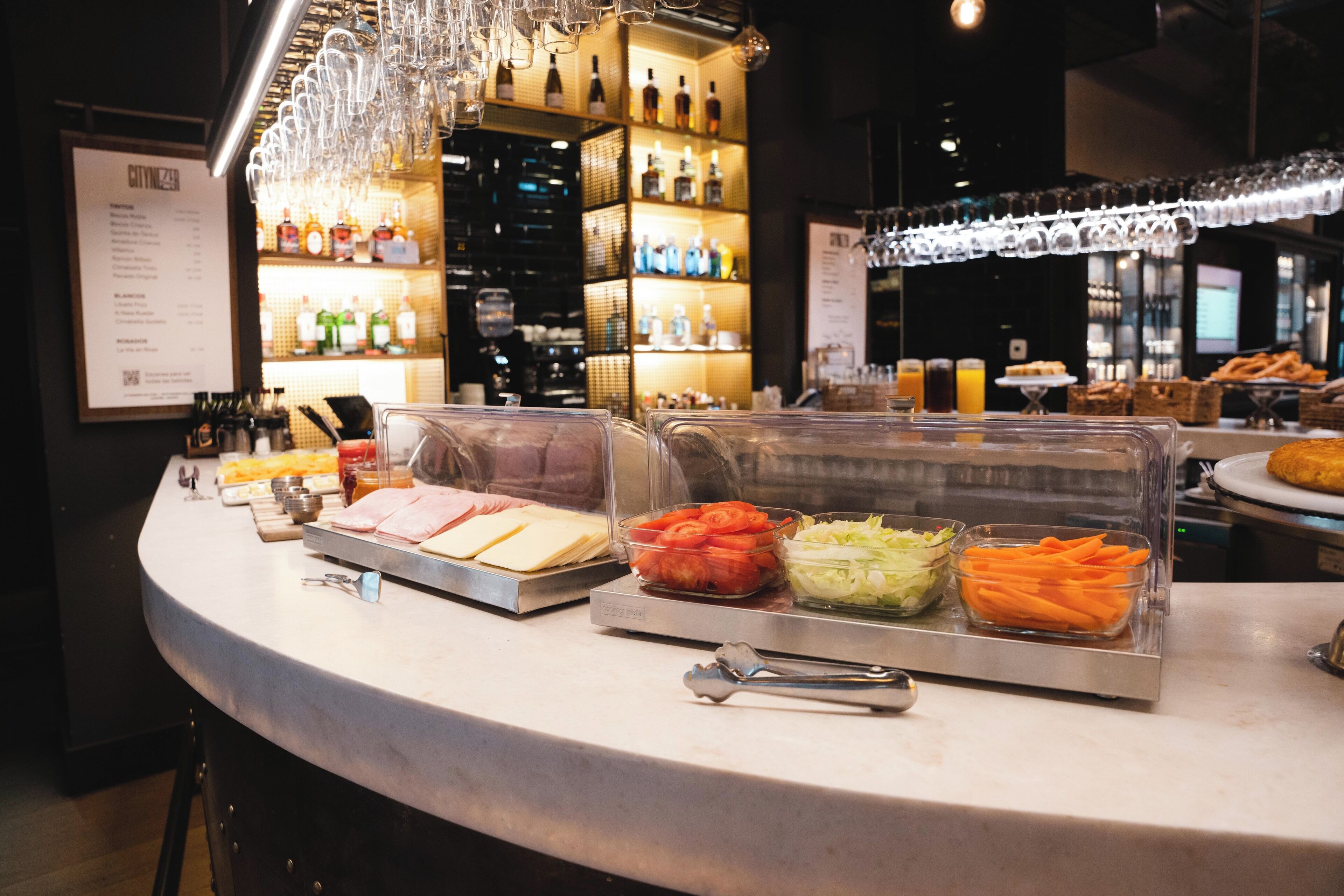 Un mostrador de buffet con diversos alimentos y una zona de bar con estantes llenos de botellas.