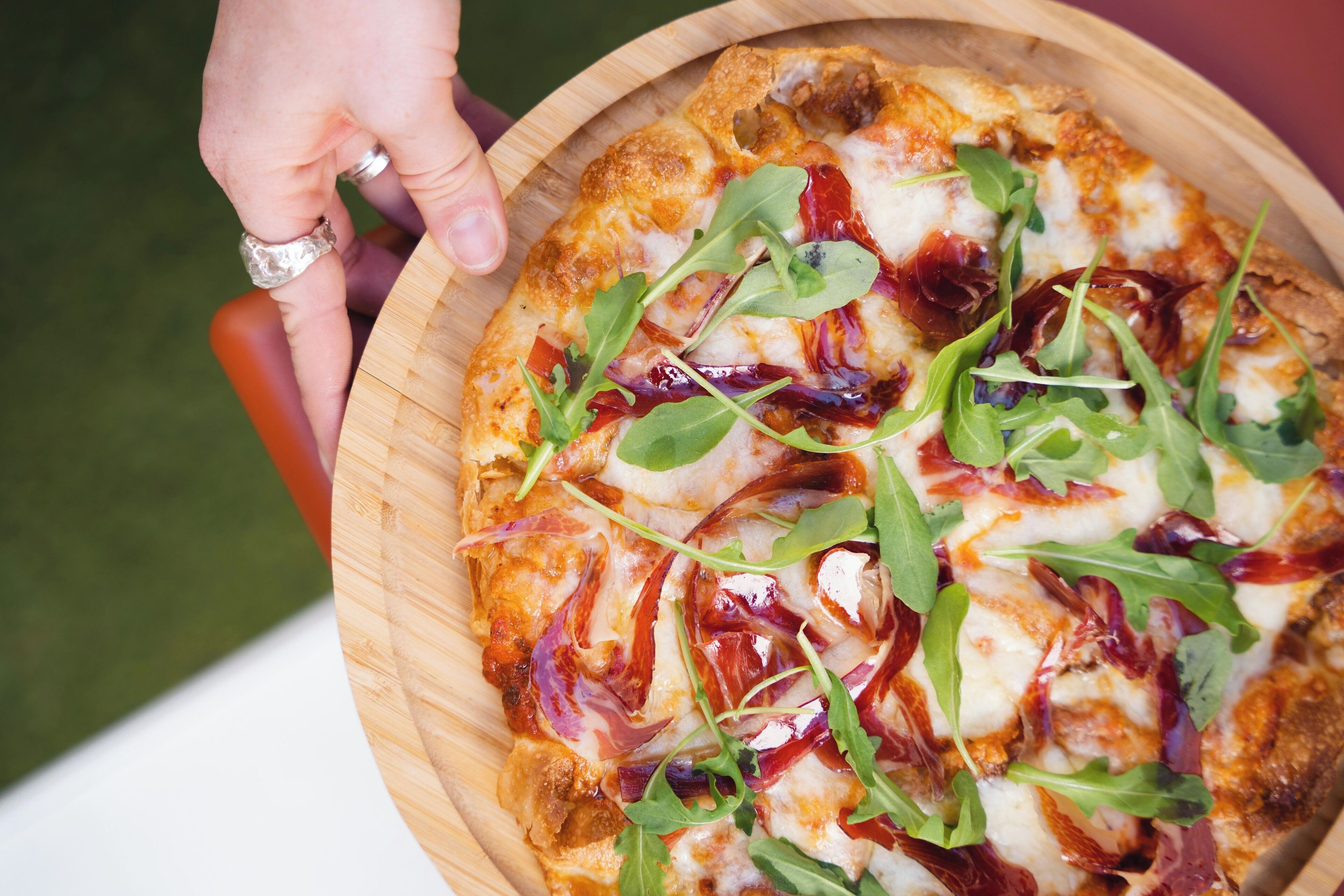 Pizza, jonka päällä on rucolaa ja ilmakuivattua kinkkua, tarjoiltuna puulevylle.