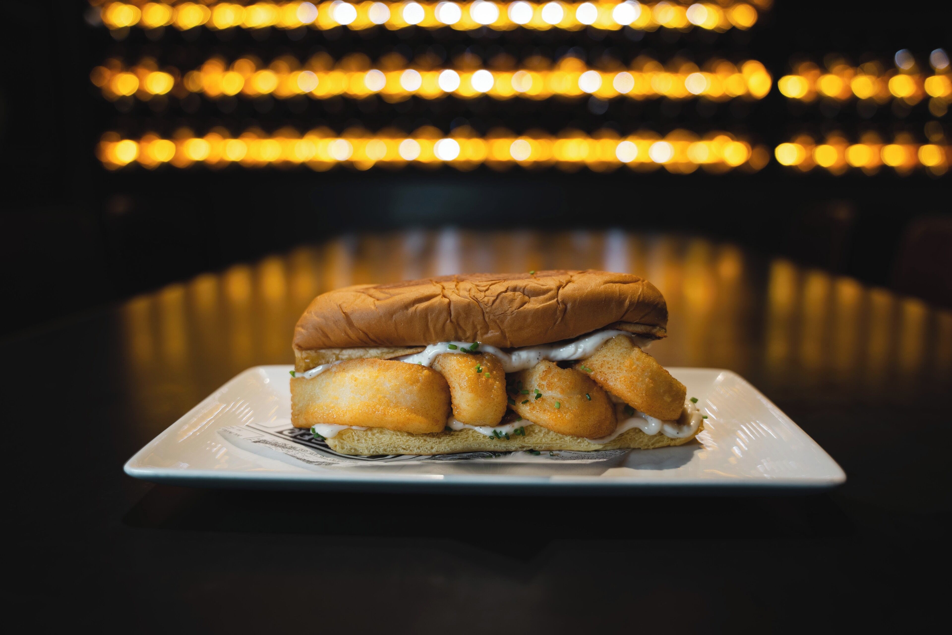 A sandwich on a white plate with a blurred background of lights.