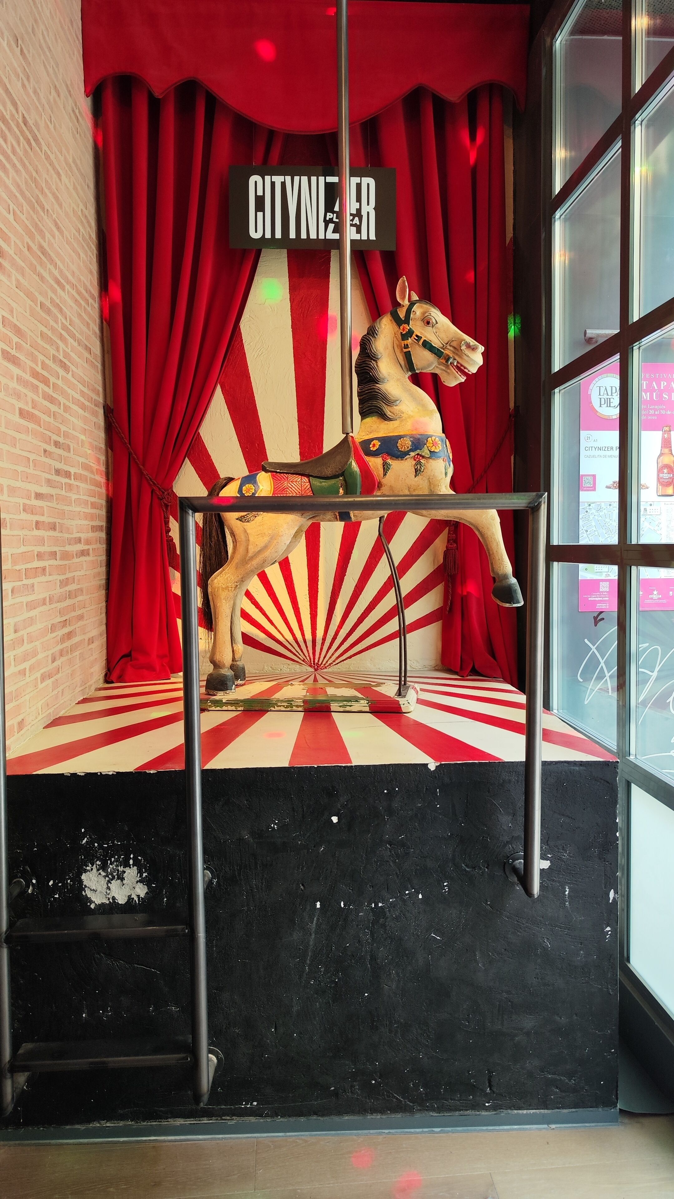 A carousel horse sculpture in a room with red curtains and a sign that reads "CITYNIZER."